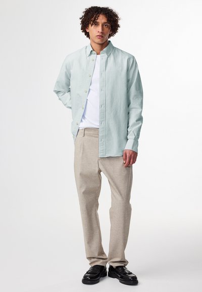 Camicia azzurro chiaro a righe con colletto, abbinata a pantaloni beige e scarpe nere. Presenta maniche lunghe e chiusura con bottoni frontali.