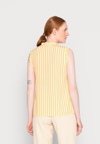 Top sem mangas amarelo e branco com gola de babados. Feito de tecido leve, apresenta um corte reto e uma textura suave.