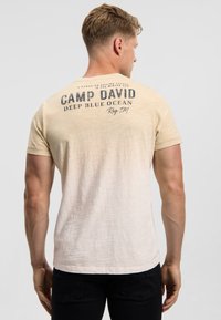 Cream gradient t-shirt with a round neckline. Features dark text on the back, including "CAMP DAVID" and "DEEP BLUE OCEAN." Short sleeves.