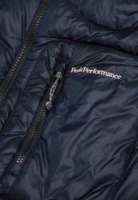 Navy insulated jacket featuring a front zip, smooth texture, and the "PeakPerformance" logo in silver on the chest area.