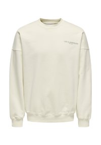 Cremfarbener Pullover aus weichem Stoff. Mit Rundhalsausschnitt, überschnittenen Schultern und kleinem blauen Text "LES CLASSIQUES" auf der Brust.