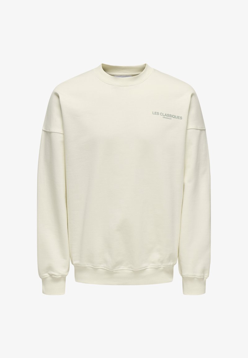 Cremfarbener Pullover aus weichem Stoff. Mit Rundhalsausschnitt, überschnittenen Schultern und kleinem blauen Text "LES CLASSIQUES" auf der Brust.