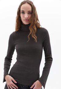 Donkerbruin langmouwige turtleneck top in een geribde textuur, met aansluitende mouwen die licht uitlopen bij de polsen.