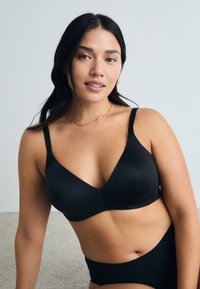 Black wireless bra with a V-neck design, made of smooth fabric. Features adjustable straps and a seamless finish for comfort.