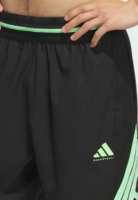 Svarta basketshorts i lättviktsmaterial, med ett grönt elastiskt midjeband och en logotyp samt ljusgröna ränder på sidan.