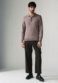 Lichtpaarse polo met lange mouwen, een kraag en knoopjeslijst, gecombineerd met donkere broeken en zwarte schoenen. Soepele textuur, casual ontwerp.