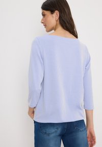 Helles blaues, geripptes Oberteil mit Dreiviertelärmeln und quadratischem Ausschnitt. Kombiniert mit blauen Jeans, was einen lässigen Stil zeigt.
