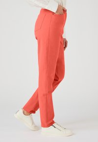Koraalkleurige katoenen broek met een rechte snit, voorzakken en zijnaad, gecombineerd met witte sneakers met textuuraccenten.