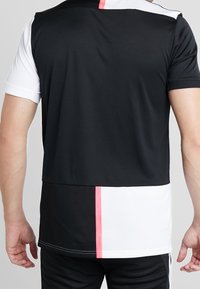 Camiseta atlética en blanco y negro con manga corta, que presenta una división horizontal y una franja vertical rosa en la parte posterior. Material suave y ligero.