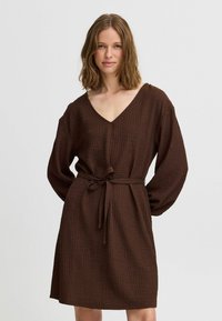 Robe enveloppante marron texturée avec un décolleté en V, des manches longues et une ceinture à nouer à la taille. Tissu tissé avec un motif à quadrillage subtil.