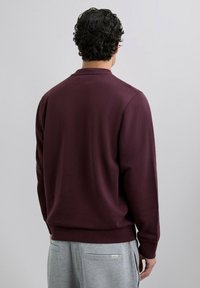 Bordeaux sweatshirt med rund halsudskæring og ribstrikkede manchetter, vist bagfra. Parret med lysegrå sweatpants med baglomme.