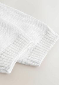 Bela pletenina z teksturiranim vzorcem in rebrastimi manšetami. Gladek zaključek, mehak otip in enotno šivanje skozi vse.