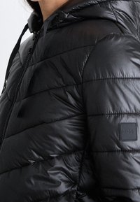 Czarna kurtka puchowa z kapturem, z pikowanym wzorem, błyszcząc�ą fakturą i naszywką z logo po lewej stronie. Zamek błyskawiczny i ściągacze.