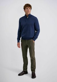 Marinefarbener Pullover mit Viertelreißverschluss, kombiniert mit olivgrünen Slim-Fit-Hosen und dunkelbraunen Slippern. Glatte Textur und lässige Passform.