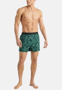 Gröna badshorts med blommönster, med elastisk midja och knappstängning. Tillverkade av lätt, snabbtorkande material.