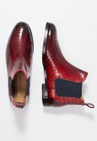 Bottines Chelsea en cuir rouge avec une texture de crocodile, panneaux latéraux élastiques et une semelle en caoutchouc noir. Présente une languette colorée.