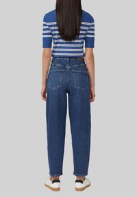Top a maniche corte a righe blu e bianche abbinato a jeans in denim scuro a vita alta e a vestibilità ampia. Tasche posteriori visibili e dettagli di cucitura.