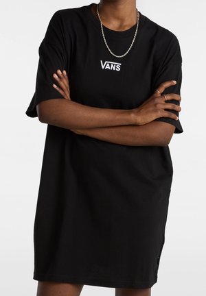 Person iført en sort Vans t-shirt kjole med armene korslagte, et sølv kædehalssmykke og to sølv ringe på højre hånd.