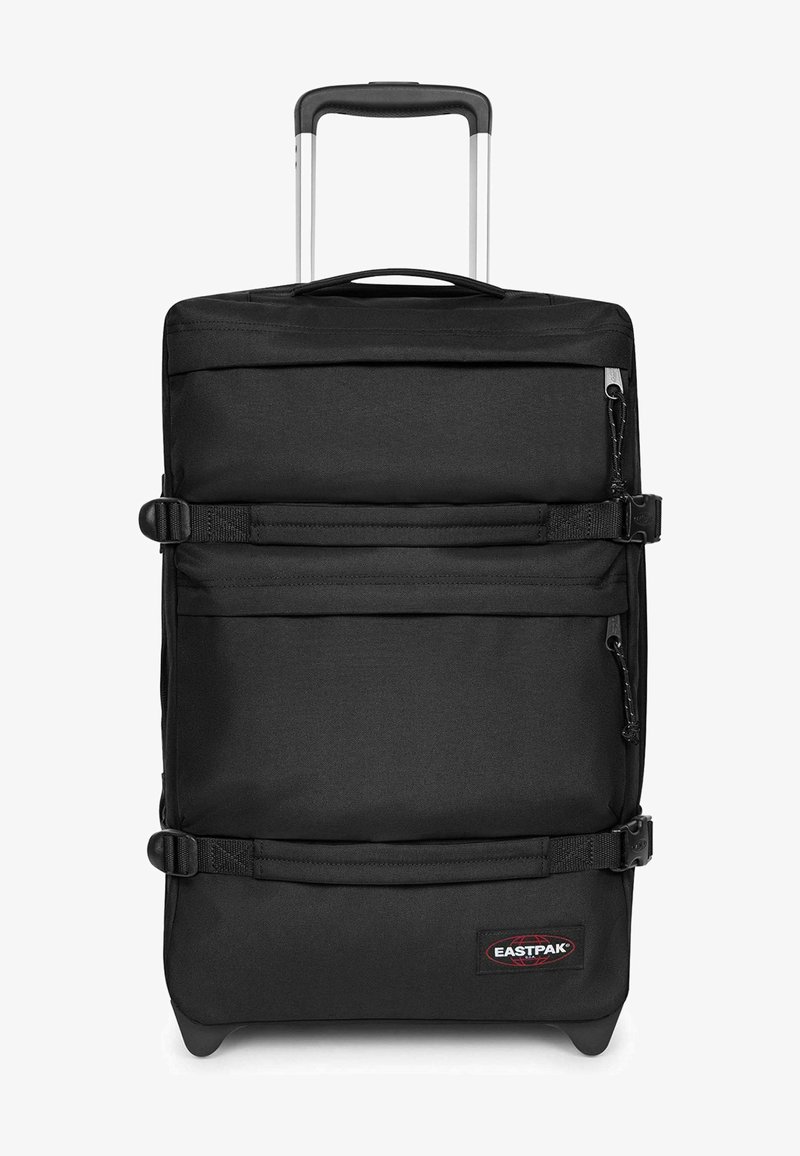 Valise noire souple, verticale, avec poignée télescopique, deux sangles de compression horizontales, poches zippées à l'avant et roulettes à la base.