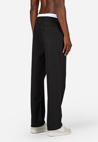 Zwarte sweatpants met een ontspannen pasvorm, gemaakt van zachte stof. Heeft een tailleband met trekkoord, een achterzak en taps toelopende pijpen.