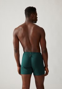 Groene katoenen shorts met een elastische tailleband, een gladde textuur en een klein label aan de achterkant, gezien van de achterzijde.