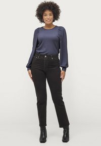 Marinefarvet, struktureret langærmet top med puffede skuldre, parret med mørkebrune tætsiddende jeans og sorte hælede ankelstøvler. Enkel, tætsiddende design.