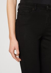 Černé džíny s úzkým střihem, které mají pět kapes, jemné švy a pás se skrytými poutky na opasek.