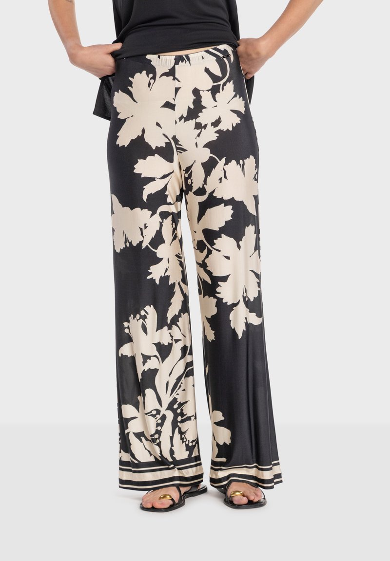 Pantalon noir à jambes larges avec un motif floral crème, en tissu lisse. Présente une coupe décontractée et un détail de ourlet rayé.