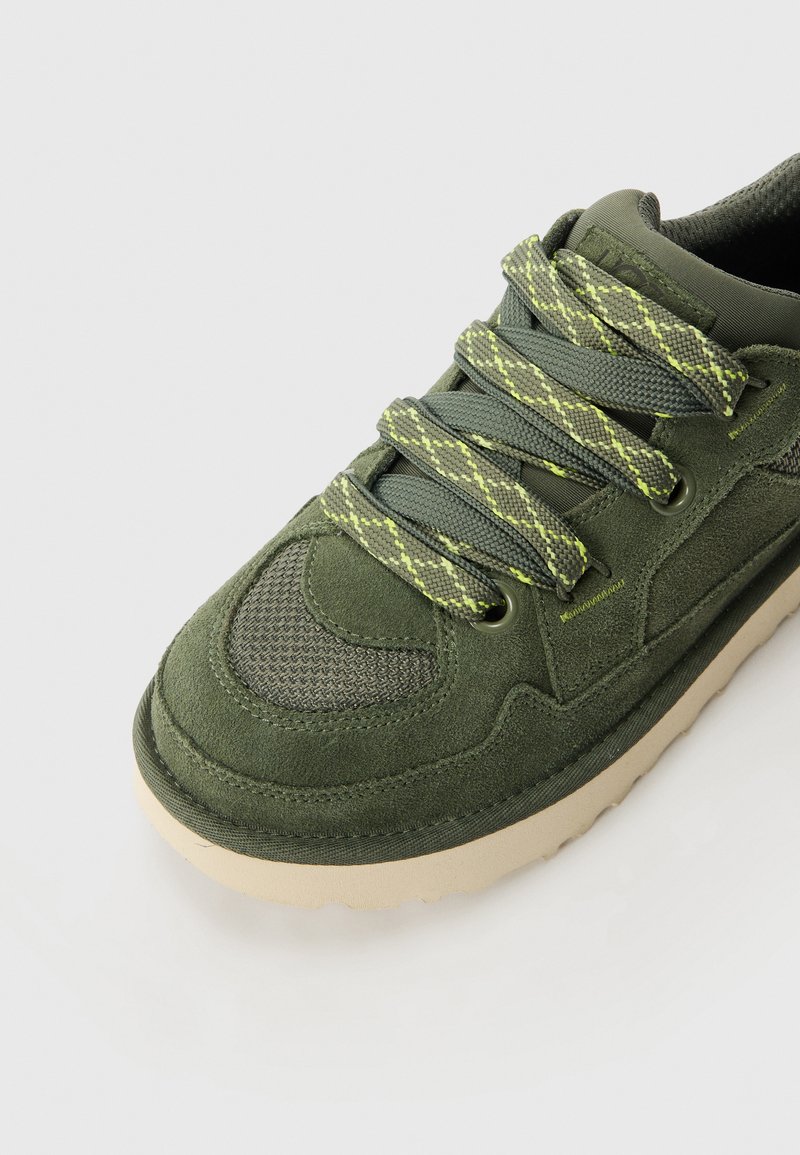Zielone zamszowe i siateczkowe sneakersy z fakturowaną cholewką, szarymi sznurowadłami z żółtymi akcentami oraz kontrastującą jasnobeżową podeszwą.