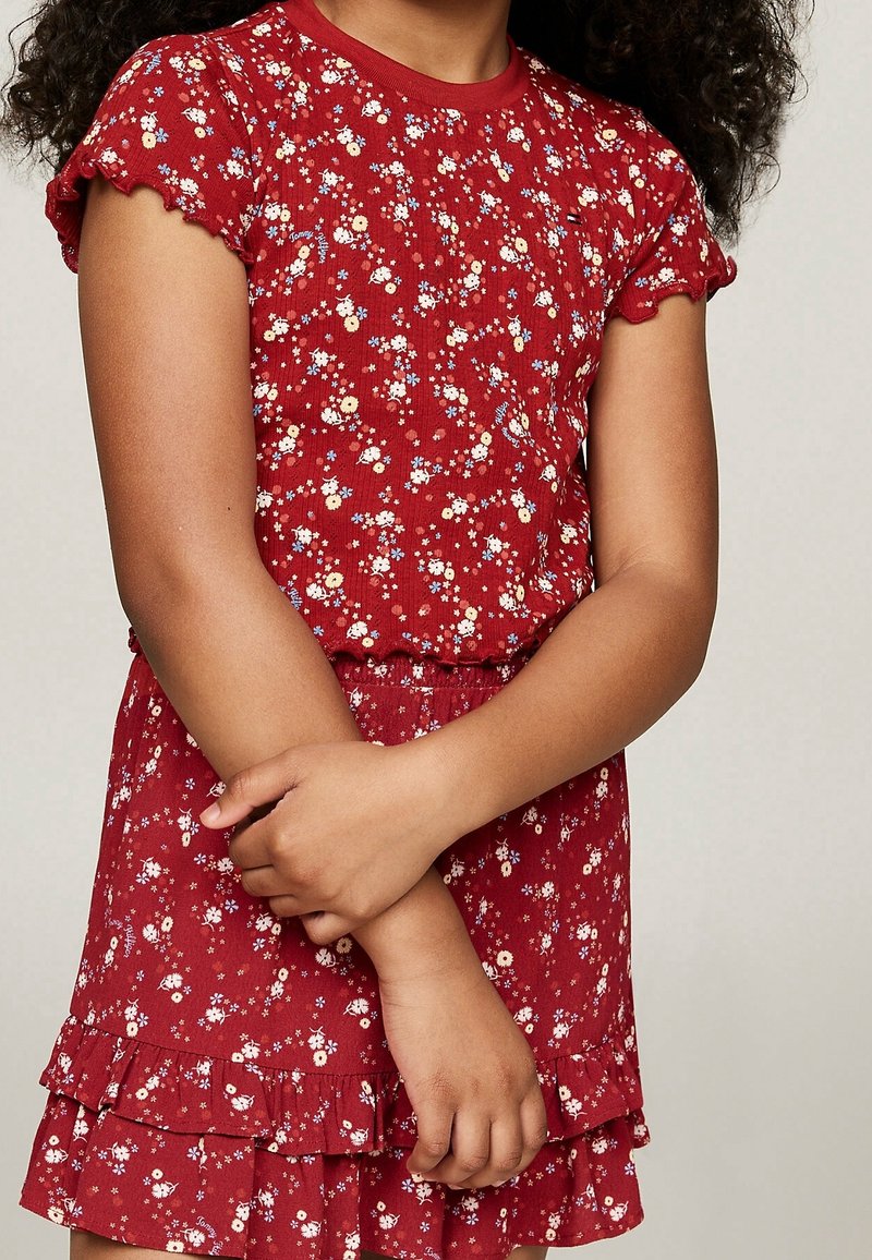 Rotes Kleid mit Blumenmuster, kurzen, gerafften Ärmeln und einem schichtweisen Rock. Hergestellt aus strukturiertem Stoff; verfügt über bunte Blumenakzente.