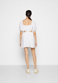 Vit kort klänning med fyrkantig rygg, puffärmar och sidoutskärningar. Slätt bomullstyg med avslappnad passform. Bärs med knöliga beige sneakers.