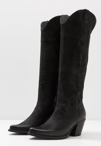 Botas de cuero negro hasta la rodilla con una textura suave, punta afilada y diseño superior curvado. Cuentan con un tacón moderado apilado.