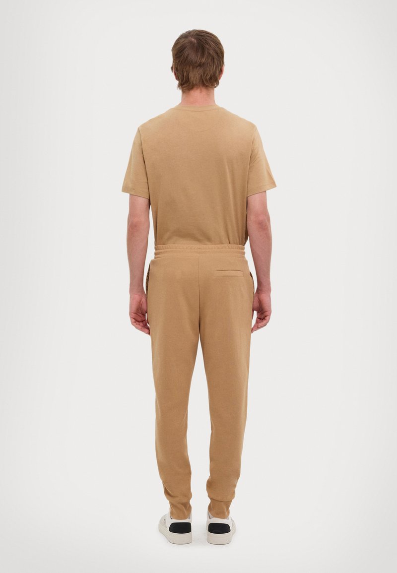 Camiseta de algodón beige y joggers a juego con un ajuste relajado. Los joggers cuentan con una cintura elástica y un bolsillo trasero.