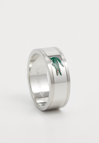 Bague en métal argenté avec une finition lisse, présentant un logo de crocodile vert et rouge au centre de la bande. Design simple et moderne.