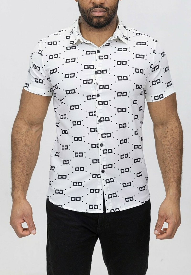 Chemise blanche à manches courtes avec des motifs géométriques noirs, avec un devant boutonné et une texture de tissu lisse. Portée avec un pantalon noir.