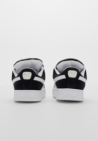 Czarne zamszowe trampki z białą gumową podeszwą, z wyściółką w kołnierzu, logo Puma na pięcie oraz białymi paskami po bokach.
