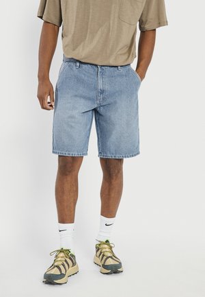 Light blue denim shorts with a straight cut, featuring five pockets. Paired with a beige T-shirt and multi-tone sneakers.