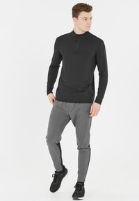 Sort langærmet top med halv-zip design, parret med lys grå tapered bukser med sorte sideakcenter og sorte atletiske sko.