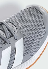 Zbliżenie na szaro-sportowe buty z siateczkowego materiału, szarymi sznurówkami, białymi paskami po bokach oraz białą podeszwą z gumowym brzegiem.