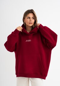 Hoodie oversize bordeaux con tasca a marsupio, caratterizzato da testo ricamato bianco "Sii unico, sii te stesso", realizzato in morbido materiale misto cotone.