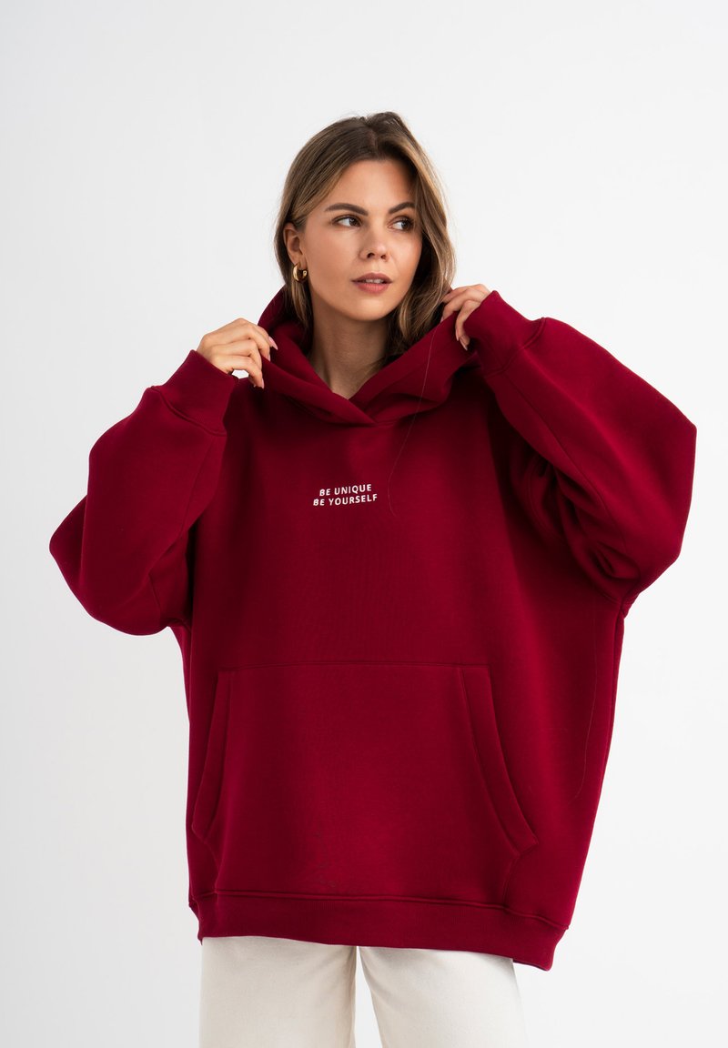 Hoodie oversize bordeaux con tasca a marsupio, caratterizzato da testo ricamato bianco "Sii unico, sii te stesso", realizzato in morbido materiale misto cotone.