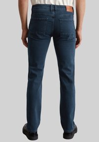 Donkerblauwe denim jeans met een rechte snit, voorzien van twee achterzakken en een bruine leren patch op de tailleband. Stijlvolle textuur.