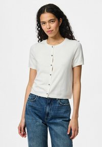 Lätt kortärmad vit cardigan med rund halsringning och silverknappar framtill, tillverkad av mjukt tyg och tillsammans med blå jeans.