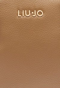 Cuir tan avec une finition texturée, arborant le logo de la marque "LIU•JO" embossé en doré, centré vers le haut.