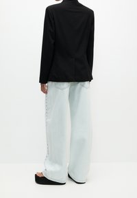 Blazer noir ajusté à manches longues, associé à un jean large bleu clair avec un détail bouton sur le côté et des sandales noires à plateforme.