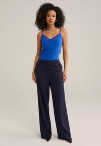 Blå linne med spetsdetaljer som matchar med marinblå vida byxor. Slät textur, figursydd upptill, utvidgning från midjan, med knappstängning.