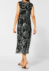 Černé šaty s bílými botanickými vzory, bezrukávový design, přiléhavý korzet a splývavá sukně až po kotníky. Hladká textura látky.