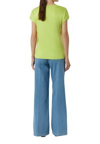 Jasnozielona, krótko rękawowa bluzka z okrągłym dekoltem, w zestawieniu z wysokim stanem, szerokimi niebieskimi dżinsami. Gładka faktura materiału.