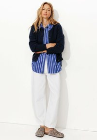Cardigan en tricot marine, chemise rayée bleue et blanche, pantalon blanc et chaussures en toile à imprimé léopard. Design simple, texture douce et coupe décontractée.