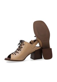 Beige offene Schuh mit Absatz, aus strukturiertem Leder gefertigt, mit Schnürung an der Vorderseite und einem mittelhohen Blockabsatz. Braune Gummisohle mit rutschfester Musterung.